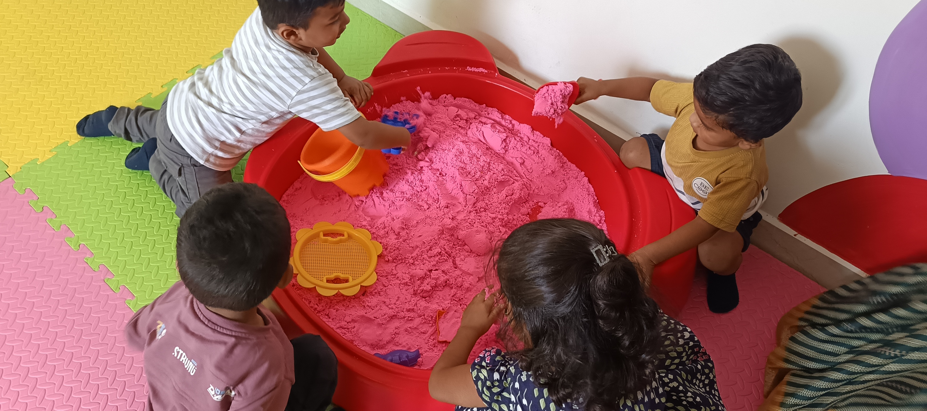 Kids molding shapes in bright pink sensory sand